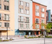 Colorful, modern apartment building with balconies and a vertical "Belltown Inn" sign; a few small trees and outdoor seating on a clean, empty sidewalk.