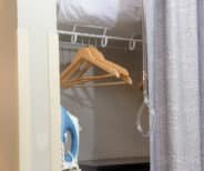 A closet with wooden hangers on a wire rack, a blue iron on a shelf below, and a gray curtain partially covering the opening.