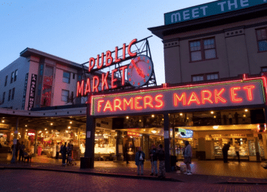 The image shows the entrance of Pike Place Market in Seattle at dusk, with neon signs for "Public Market" and "Farmers Market" glowing above people walking below.