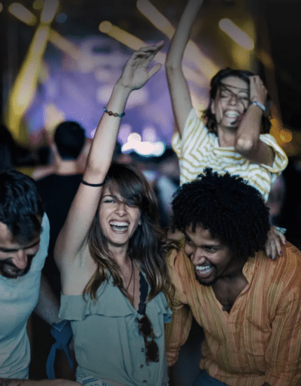 A group of people smiling and dancing together at an outdoor concert, with vibrant lights and the buzzing crowd of Events In Seattle in the background.