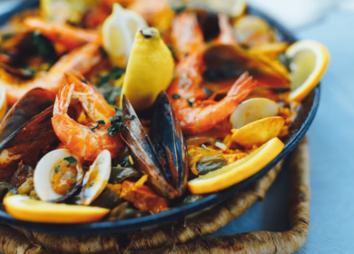 A close-up of a seafood paella featuring shrimp, mussels, clams, rice, and lemon wedges in a large shallow pan—perfect to enjoy after exploring the many Things To Do In Seattle.