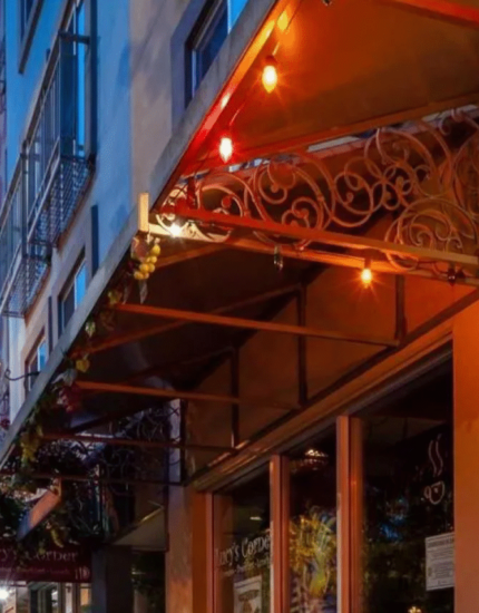 Street-level view of a building with colorful lights, metal awning, and a lit "Belltown Inn" sign at dusk; trees and city buildings visible.