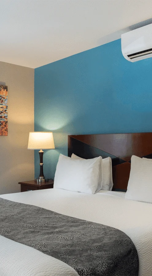 Bright hotel king room with white linens, bedside lamps, air conditioning unit, window with garden view and modern artwork — comfortable, peaceful stay
