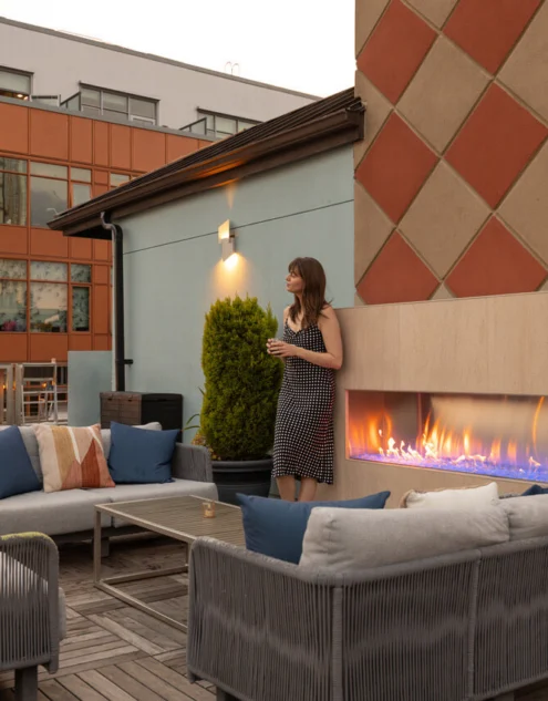 Rooftop lounge with cosy seating, modern outdoor fireplace, cushions and potted plants offering evening hotel terrace comfort for guests